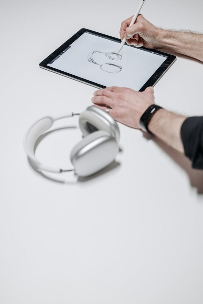 Hands sketching headphones on tablet with stylus, showcasing design process.